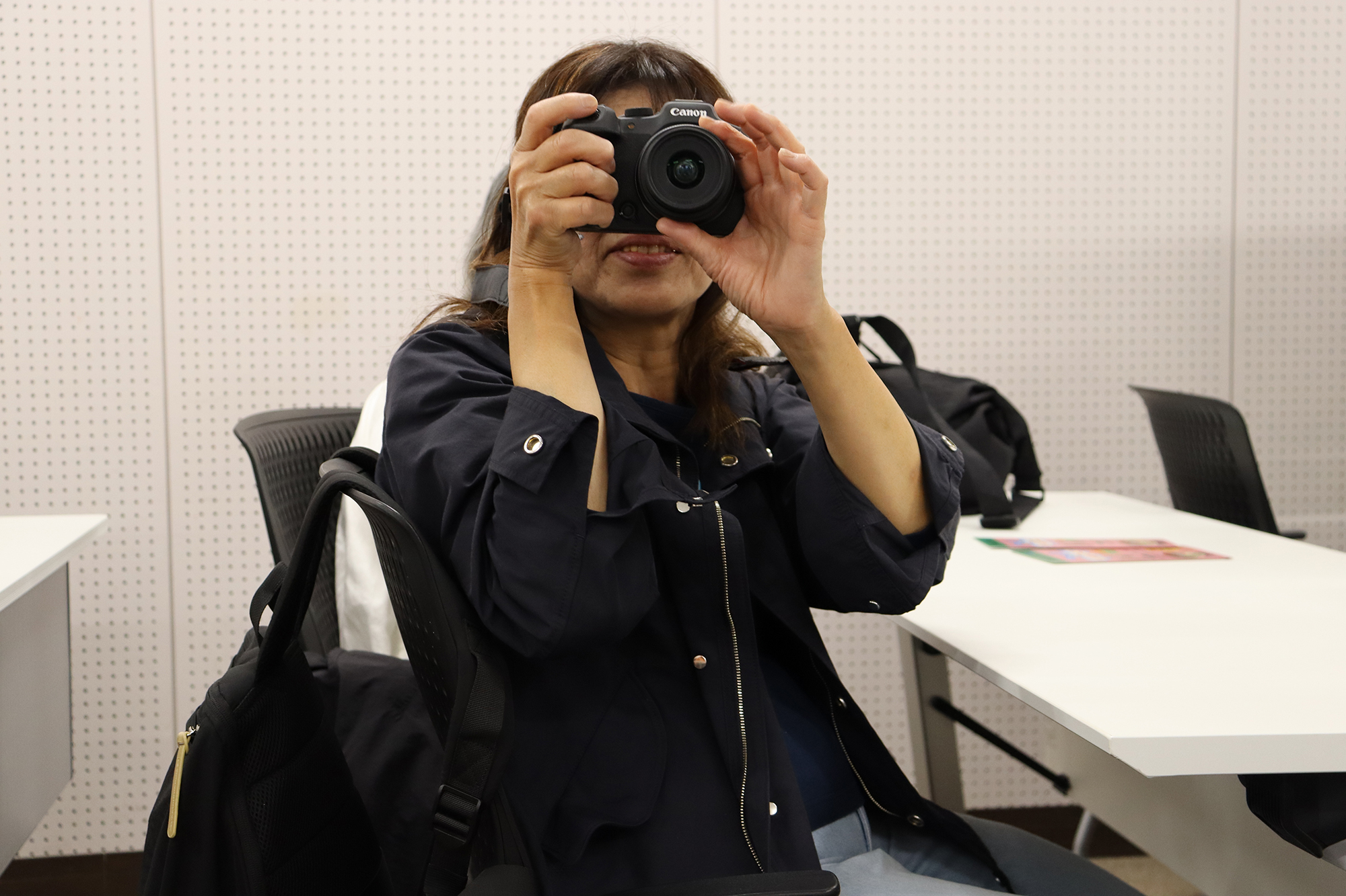 竹田さんに向けてカメラを構え、シャッターを切る海老澤さん。椅子に座りながら、両手でしっかりとカメラを支えている。