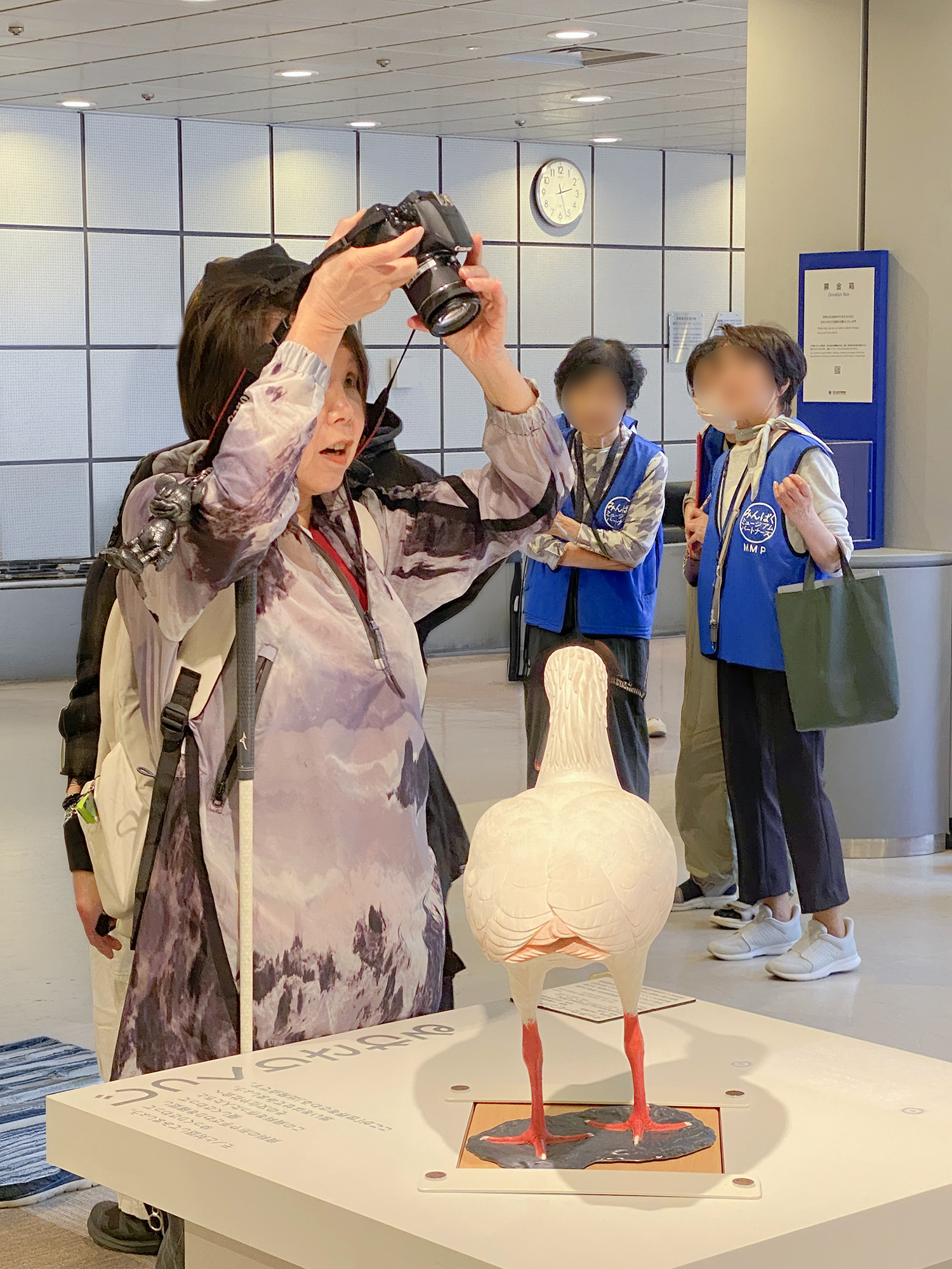 頭上にカメラを掲げ、立ったまま撮影する竹田さん。左手でレンズを支え、背後では見守るMMPの方々の姿が写っている。