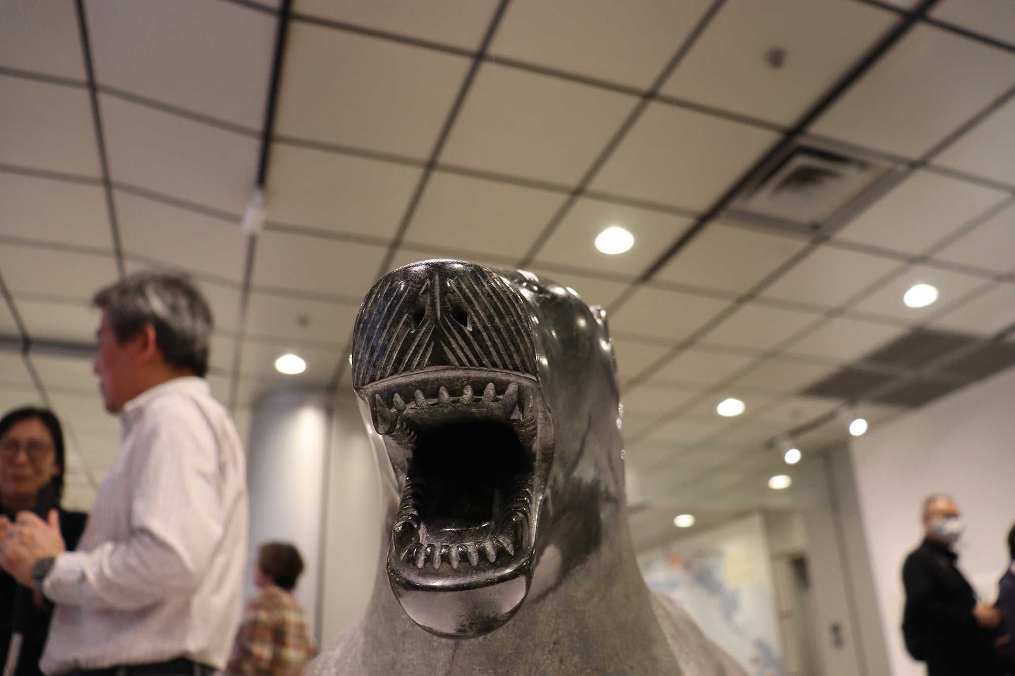 ホッキョクグマの像を少し左側から撮影した写真。口を開けた顔の奥に、会場で話をしている人たちの姿がぼけて写っている。