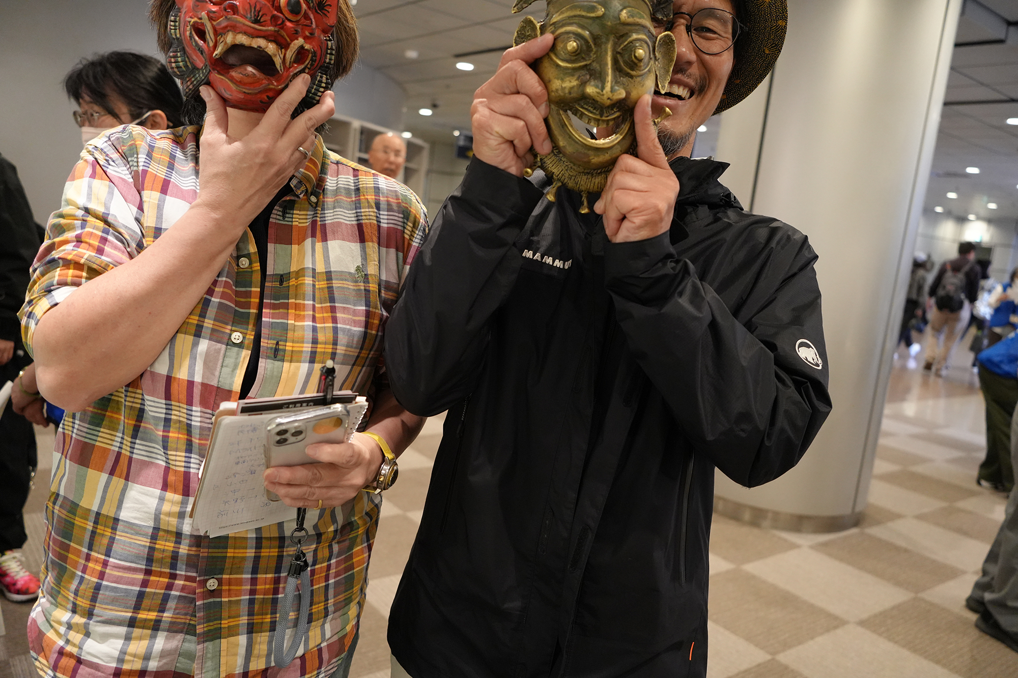 二人が仮面をつけて並んでいるが、頭の部分が画面から少し切れている写真。